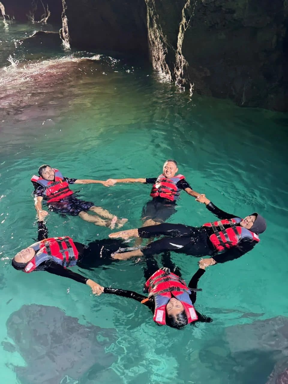 Guests floating in the turquoise pool of Bedil cave