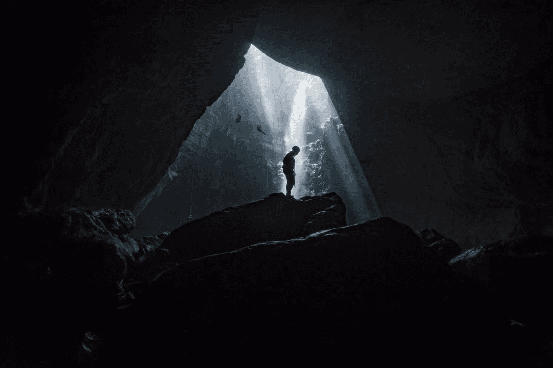 A caver rappelling in Jomblang Cave with light beams